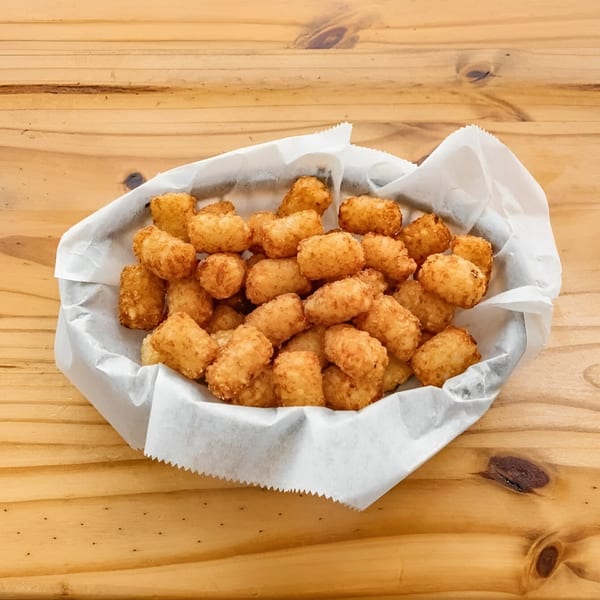 A basket of golden-brown tater tots, served in a white paper liner on a wooden table.