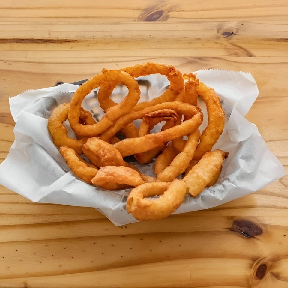 A basket of golden-brown onion rings, served in white paper on a wooden table.